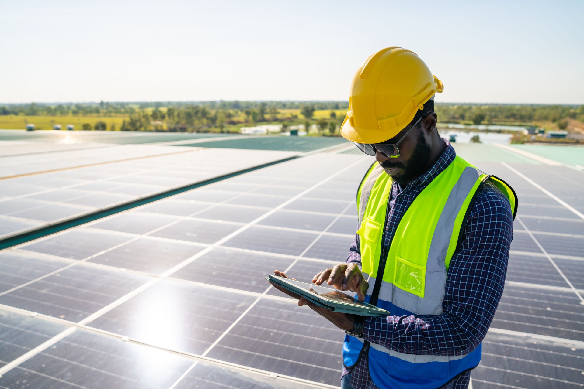African man engineer using digital tablet maintaining solar cell panels on building rooftop.